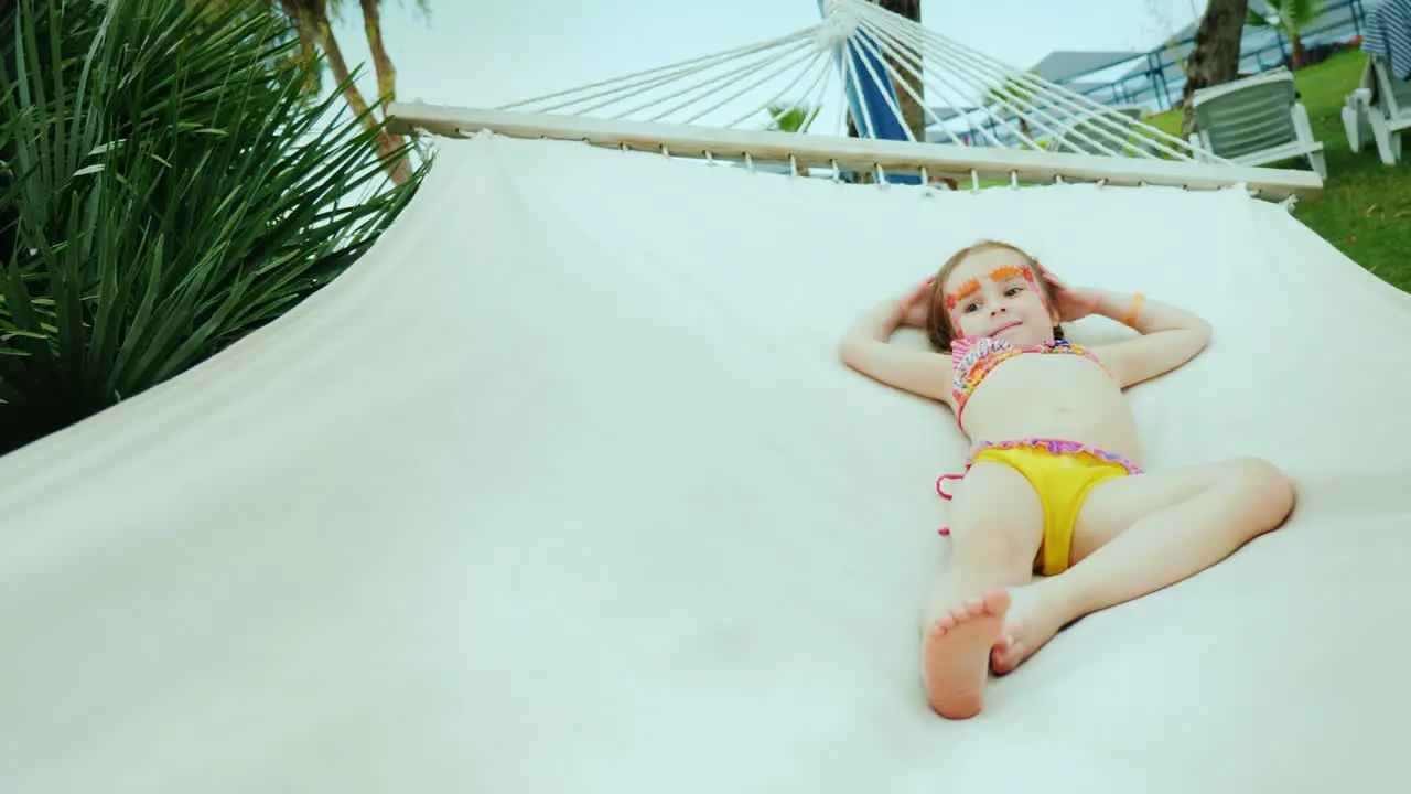 A Little Cool Girl In A Bikini With A Painted Face Rests On A Hammock During The Summer Holidays