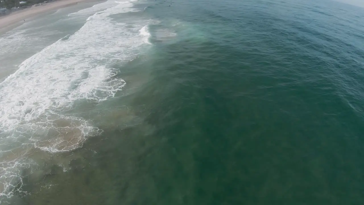 Ocean waves crash and spread white wash on sandy shore on sunny day