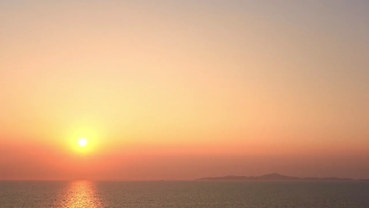 A large golden sun sets above the ocean horizon