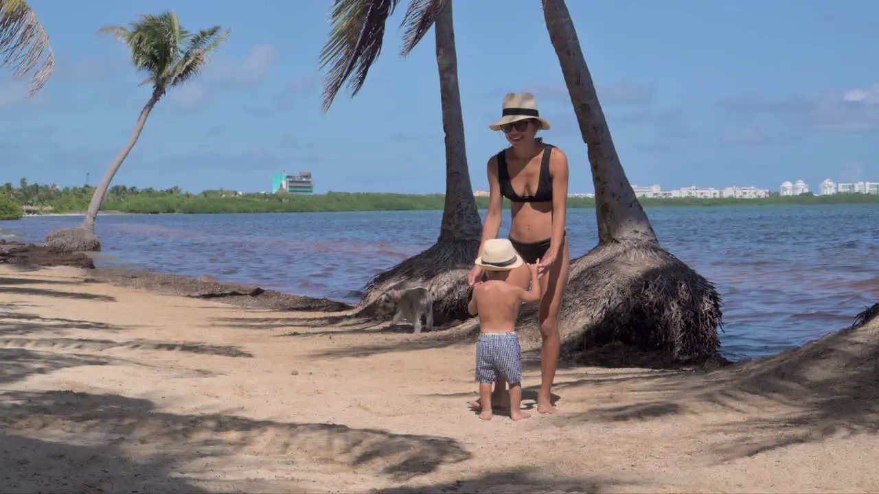 Young latin baby boy being swung around by his mother both wearing hats at the beach on a sunny day