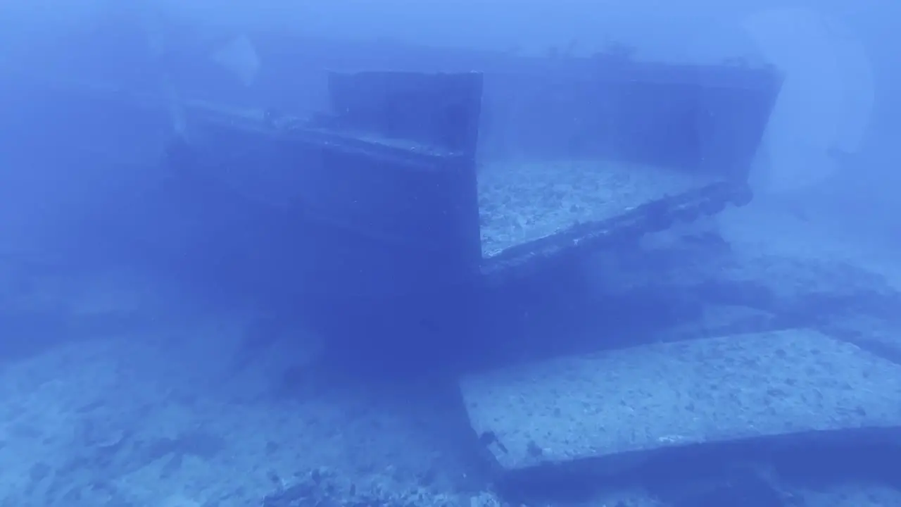 Cinematic wide shot from a submarine porthole going around the end of a shipwreck on the ocean floor off the coast of the Big Island of Hawai'i