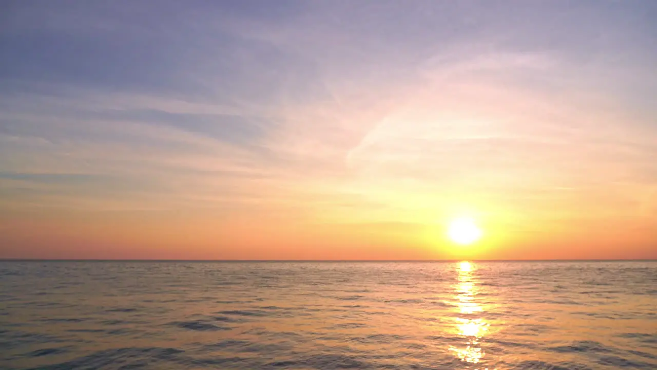 A giant yellow sun hangs on the horizon as it begins to set into the ocean waters