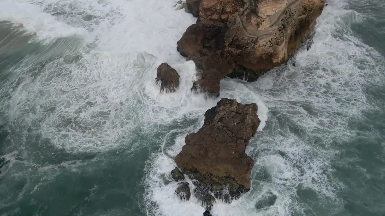 Pullback from Nazare Promontory revealing Ocean waves crashing into Rocks a Famous Surf spot In Portugal