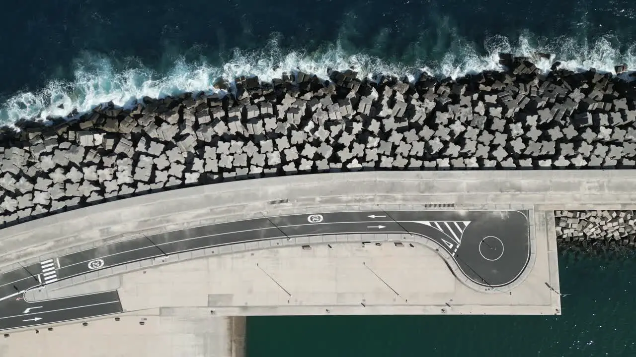 Ocean waves crash on large breakwater jetty protecting marine port and road drone top down