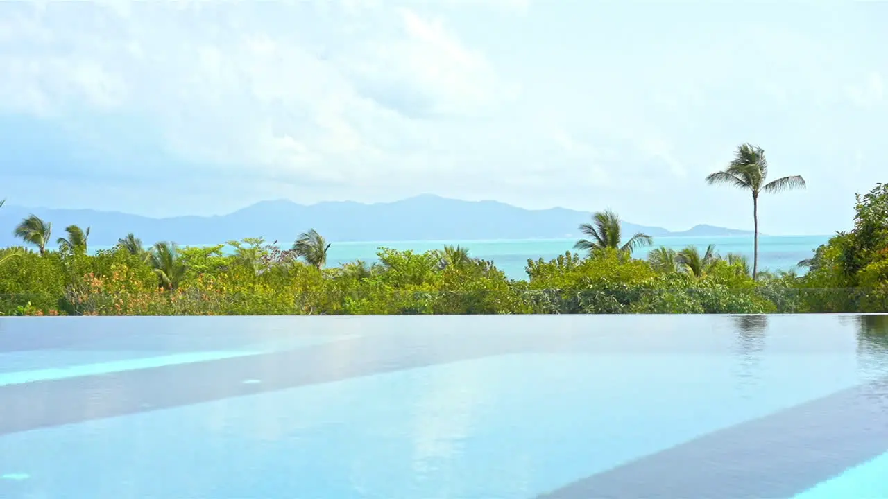 The edge of a resort infinity pool overlooks the ocean and the mountains in the distance