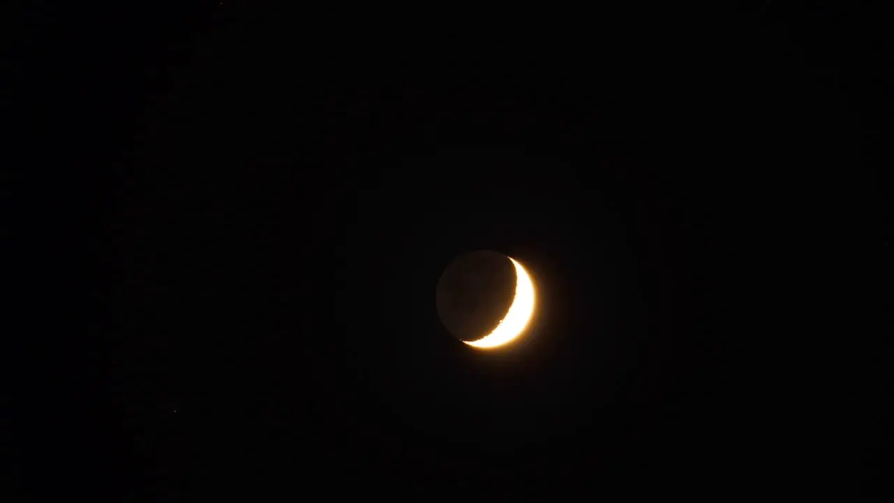 Time-lapsed tracking shot of crescent moon moving through a darkening sky at night fall