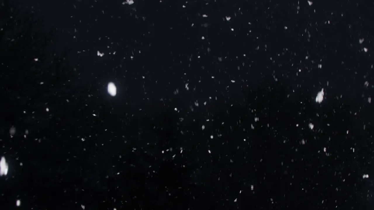 slow-motion snowfall on a dark and cold winters night panning downwards towards a snow-covered fence