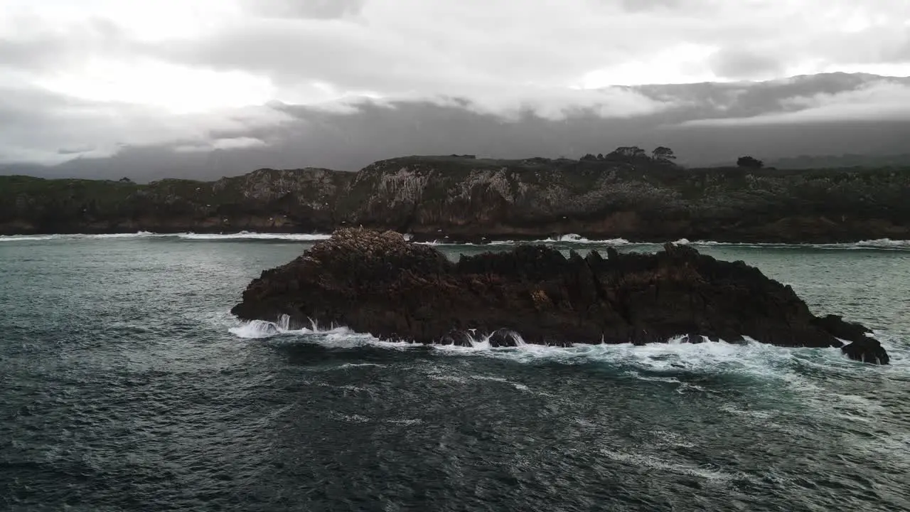 Lonely island with waves crashing on rocks and seagulls flying near shorline