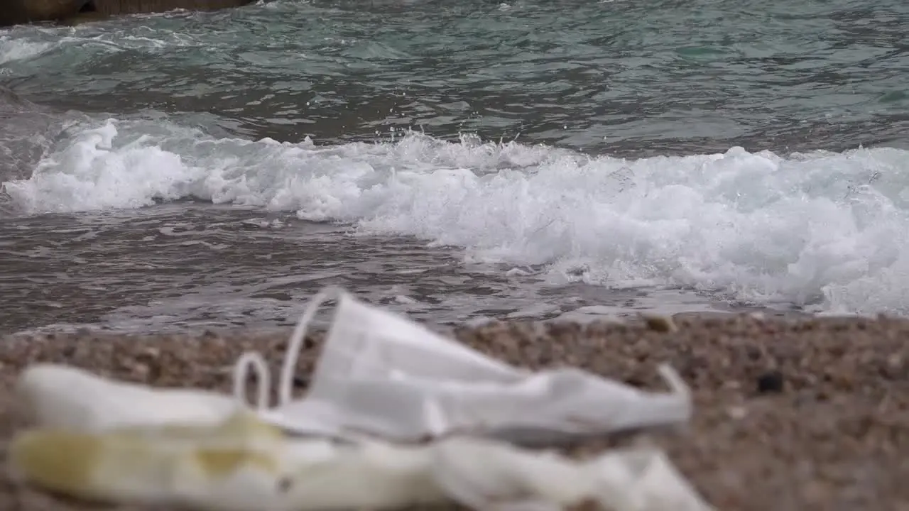 Used mask and glove left on beach with washing wave behind zoom out focusing background