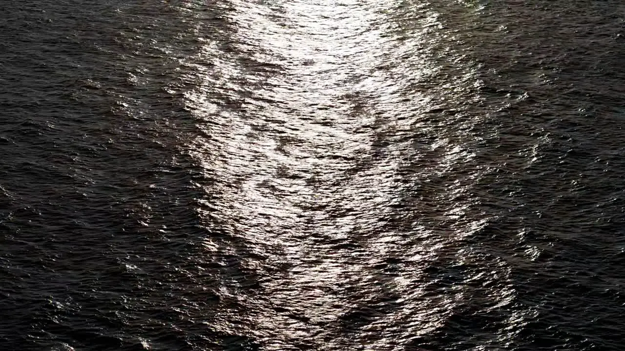 Drone push in as light glistens on leathery textured wave ripples on ocean water surface