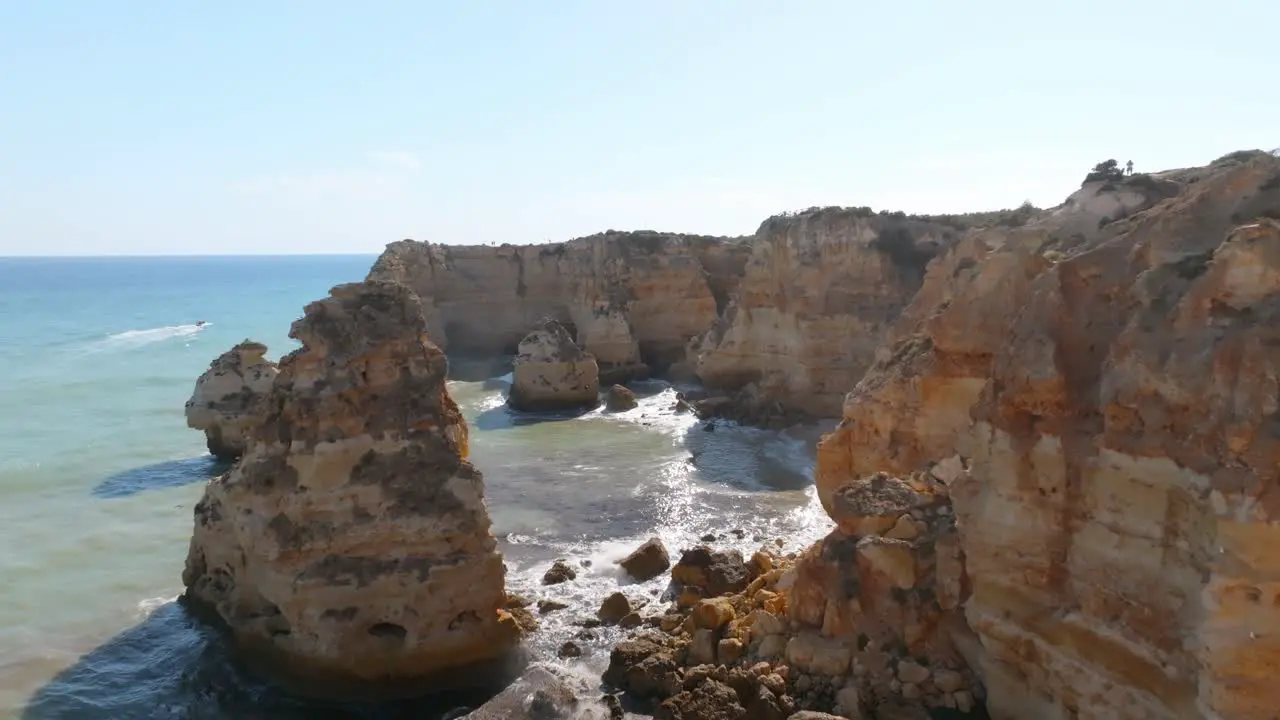 Drone pushes past rocky ocean side cliffs to reveal beautiful beaches of praia da marinha algarve portugal