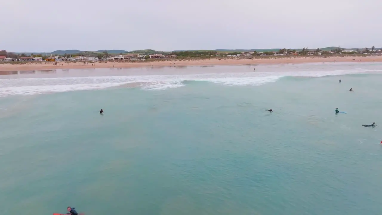 Aerial dolly to beach from open ocean water as surfers catch waves in Spain