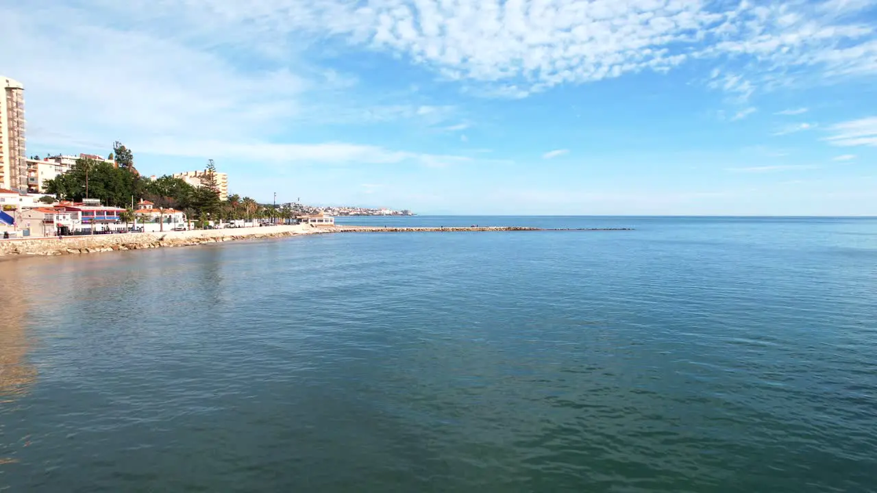 Aerial dolly towards breakwater and calm ocean waves crashing on sandy beach