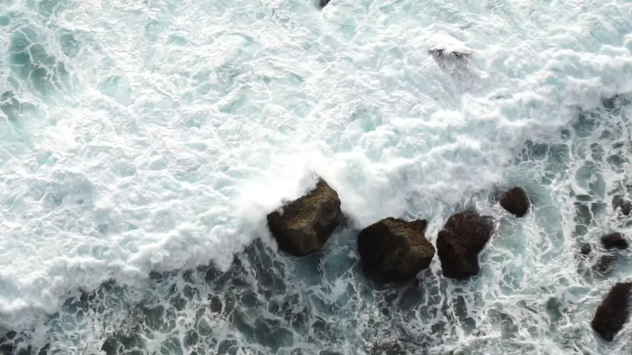 View of white ocean waves crashing into black rocky shore from above off of a cliff Bali Indonesia