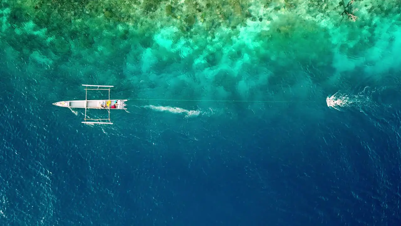 Diver ocean gliding with a Subwing in Raja Ampat Indonesia coral reef island pulled by a small motorboat Aerial top view tracking left lowering shot