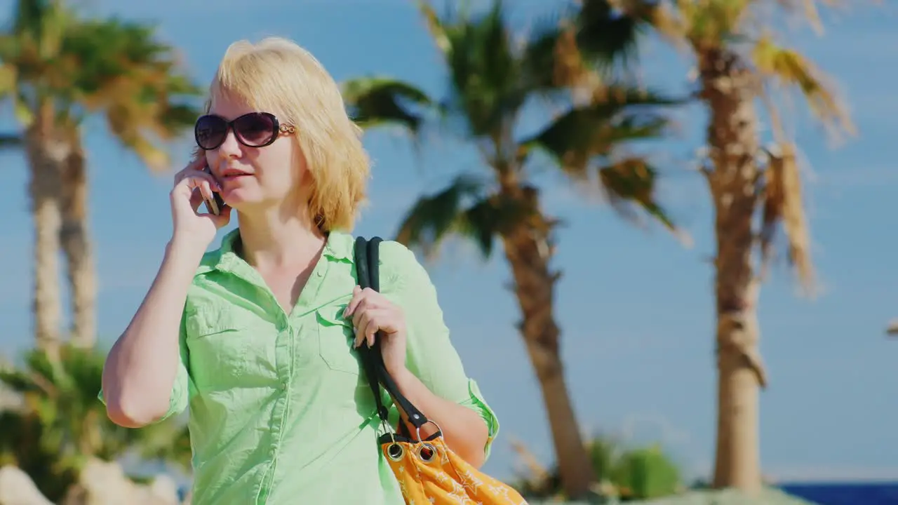 Woman Tourist In Sunglasses Talking On The Phone On The Background Of Sky And Palm Trees