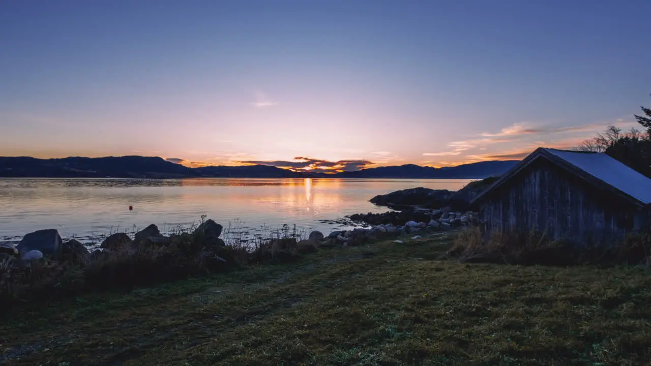 Timelapse of a sunset taken from a stony beach with a boat house in Trondheim Norway