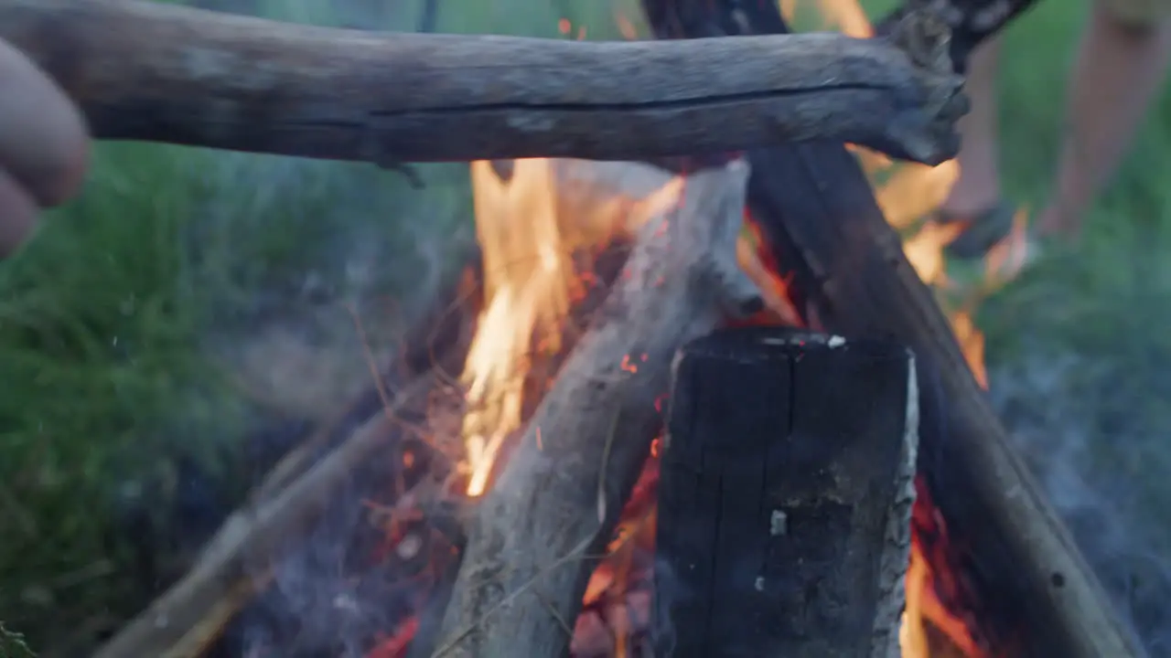 Guy Person Man adding firewood logs to Campfire Fire Burning in Dusk Evening Night in Slow Motion