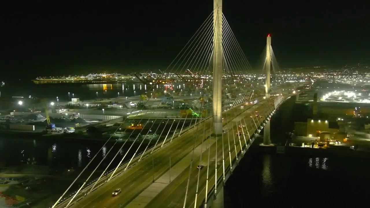 Aerial orbiting shot of lit bridge in Long Beach California | Shipping port in background