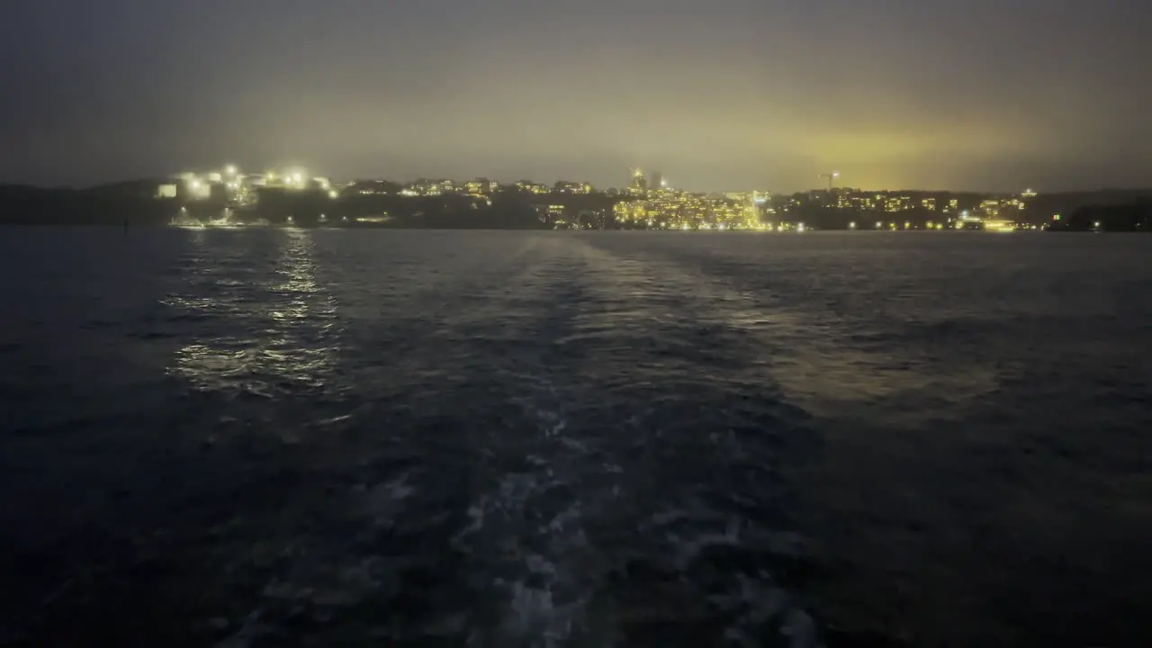 Traveling by boat during night time with the city lid up in the horizon behind the boat