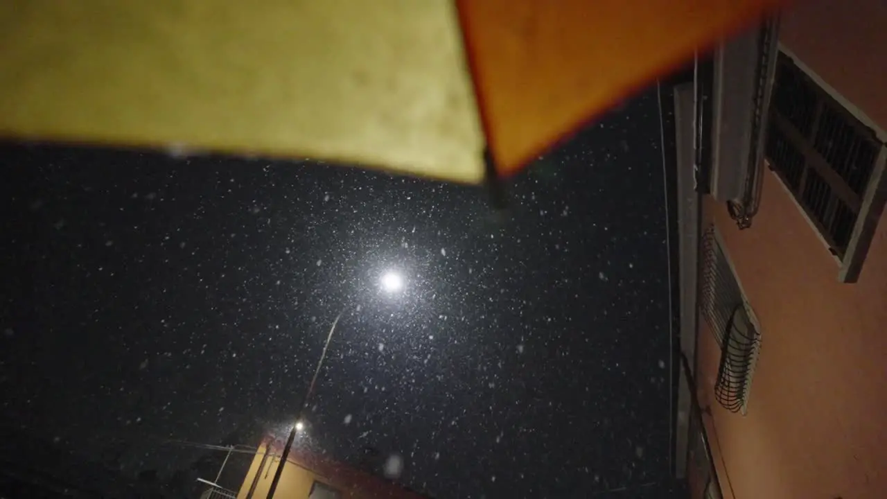 static slow motion during a snowfall in a city at night pointing at a street lamp from an umbrella