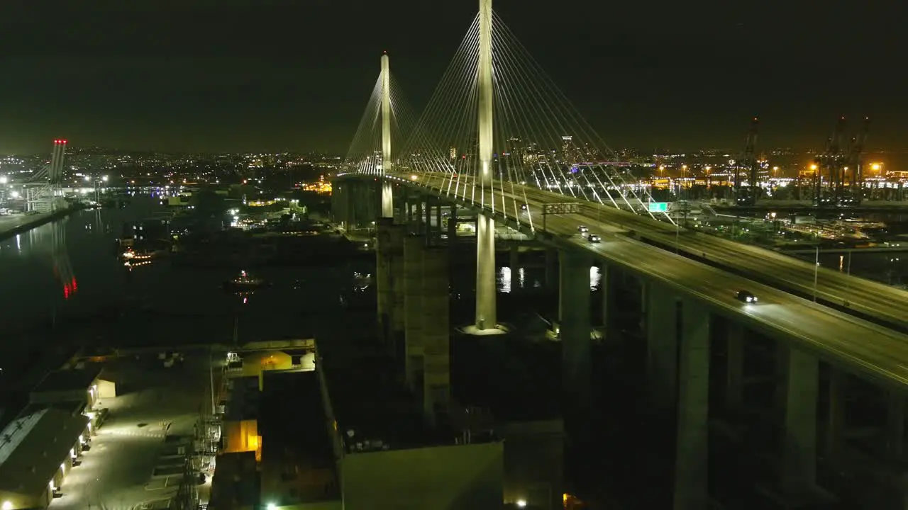 Aerial flyby of lit bridge in Long Beach California | Ship sailing underneath | Night time