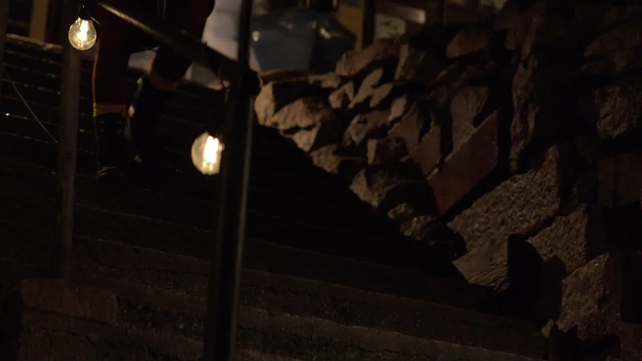 Medium wide shot of a person walking down steps at nighttime with festoon lighting