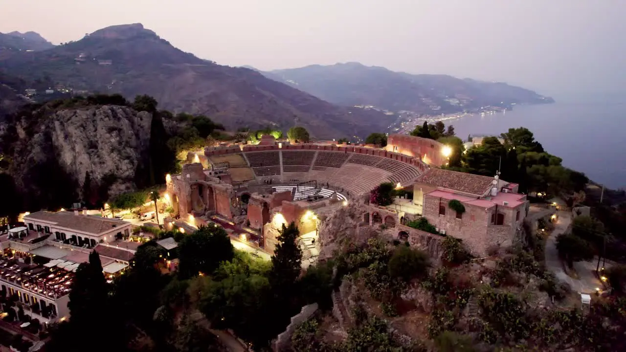 Drone orbiting around a colosseum amphitheater over Taormina's old town at night