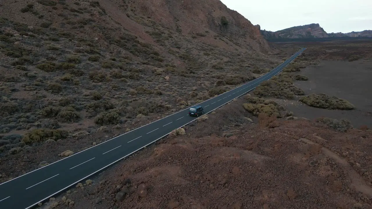 Wide Aerial Tracking Shot of Blue Van Traveling Down Highway Road with Large Mountainside Tenerife Spain