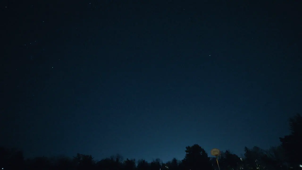 Shooting star passes through the sky over an empty basketball court at night