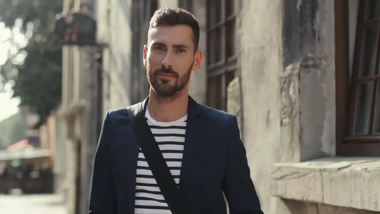 Portrait Of A Handsome Young Man In Stylish Outfit Taking Off Glasses And Smiling At The Camera In An Old Town Street