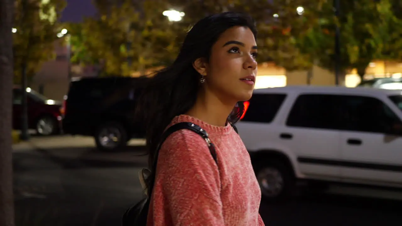 A young hispanic woman walking and shopping at stores on an urban city road under street lights at night