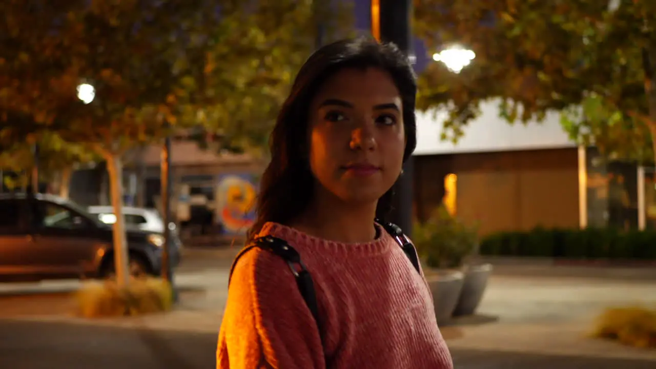 A beautiful young hispanic woman walking and shopping at stores on an urban city road under street lights at night