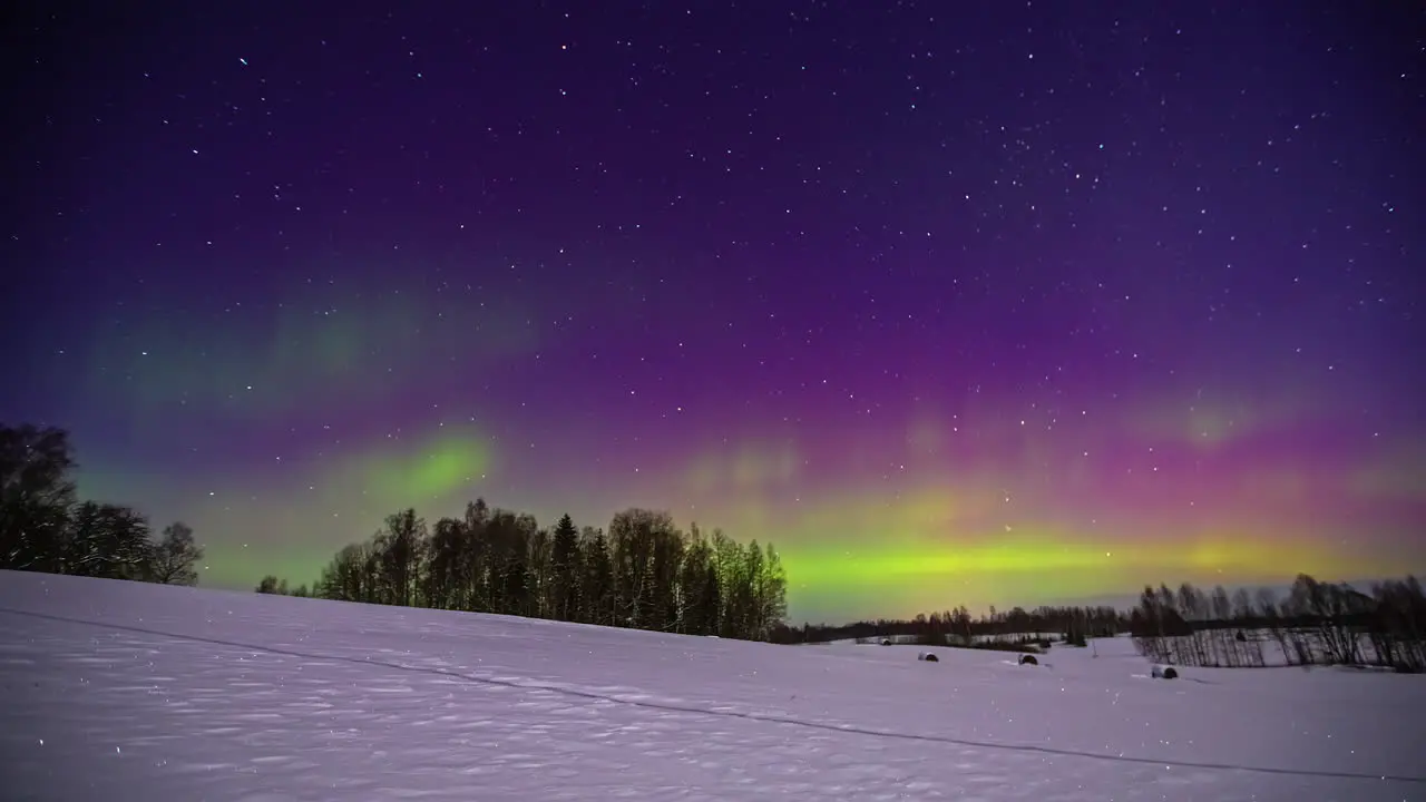 Snowy landscape and aurora borealis illuminating sky with colour changing lights