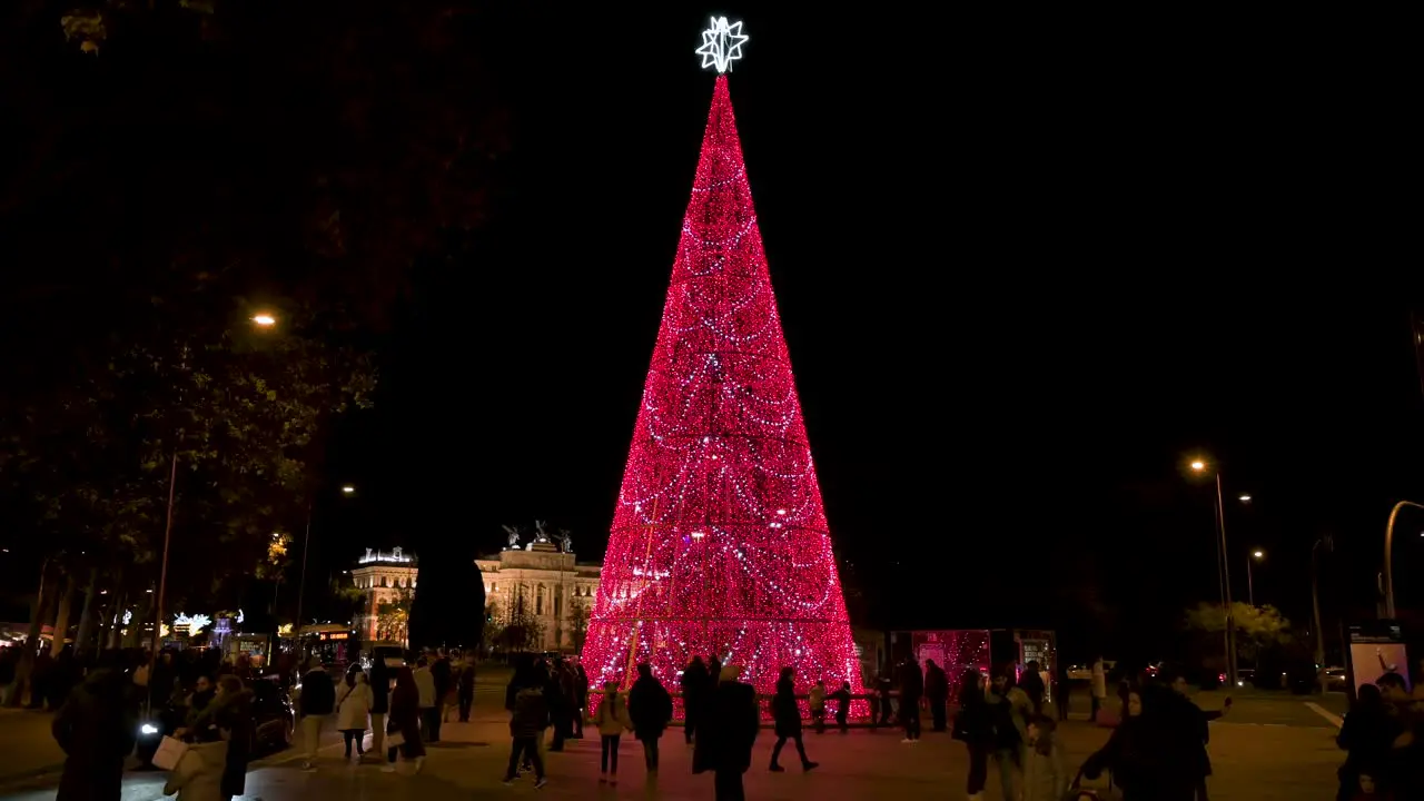 People are seen around a Christmas tree installation decorated with red LED lights for the Christmas festivities