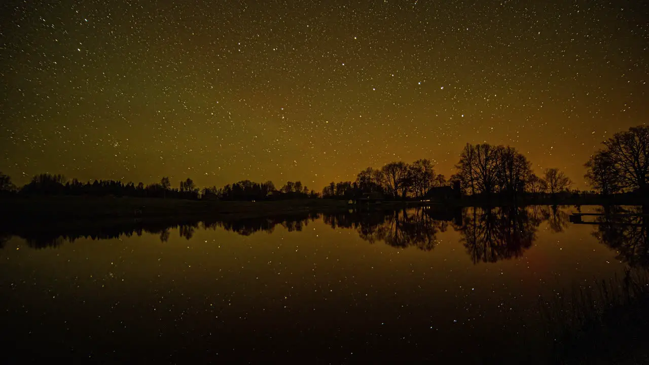 Starry night timelapse with star movement and reflection on a dark lake with trees