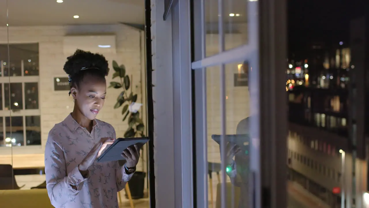 African American woman reviews data on a tablet at night in a business office