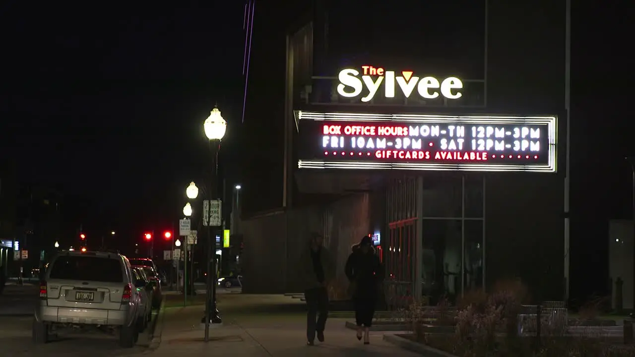 Two people walking past a music venue marquee at night