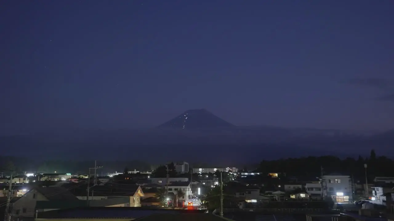 Tranquil nighttime scene showcasing the iconic Mount Fuji in Japan with a lively village below aglow with the movement of cars and vibrant night activities