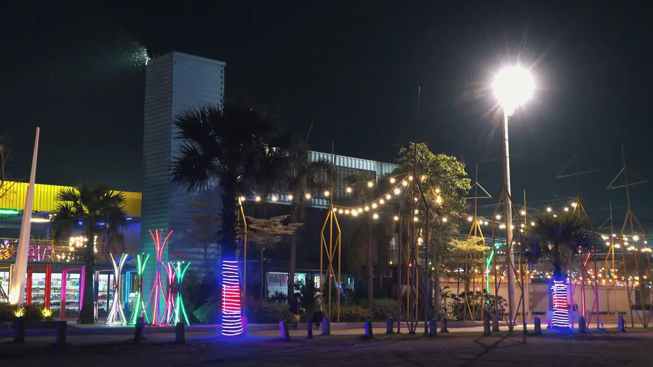 Medium still zoom out Shot Of Colorful Amusement Park made out of containers with People Walking in Front of it in the Night Time