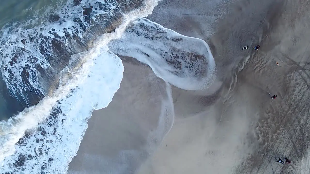 Cenital shot of the beach and the crushing waves with people walking by