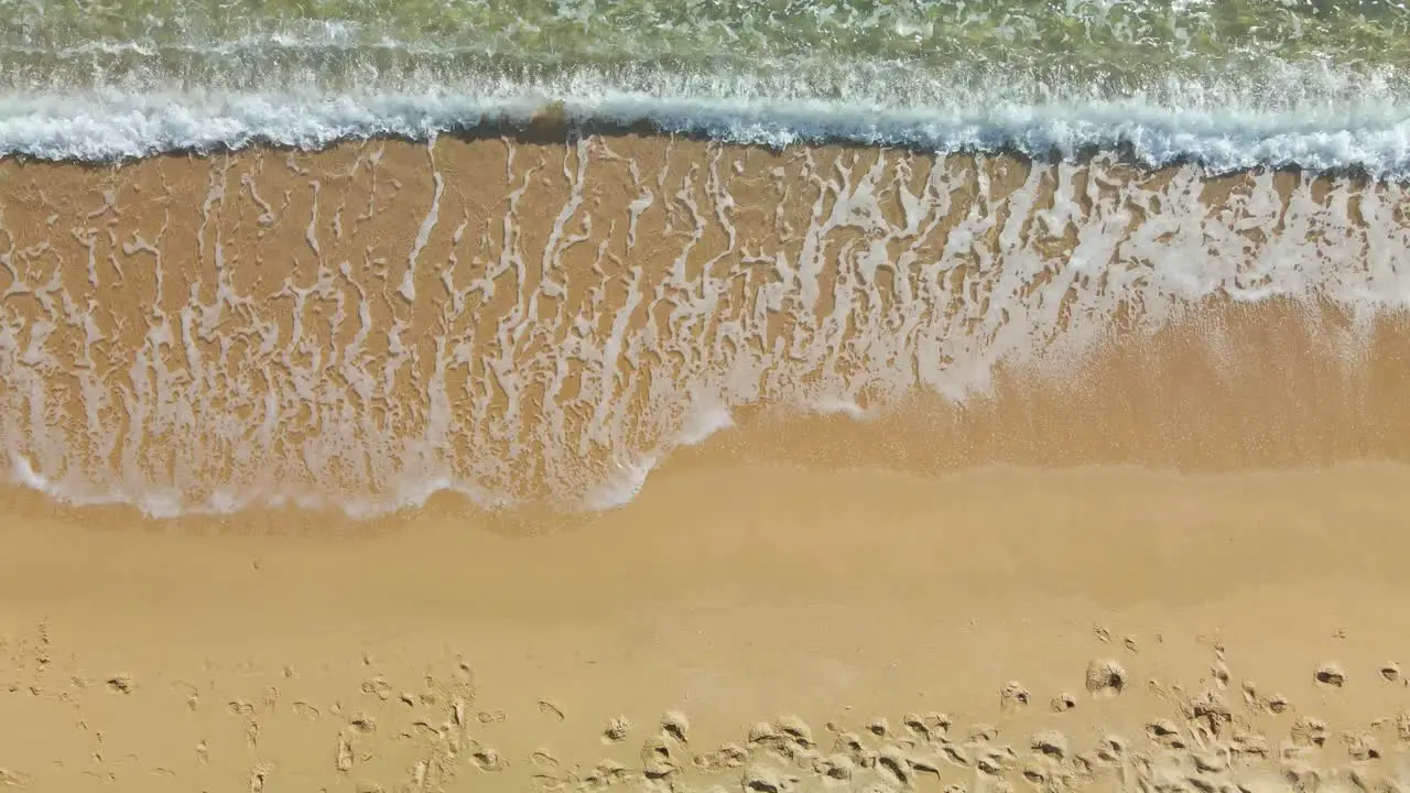 Waves rolling into a golden sand beach aerial top down view