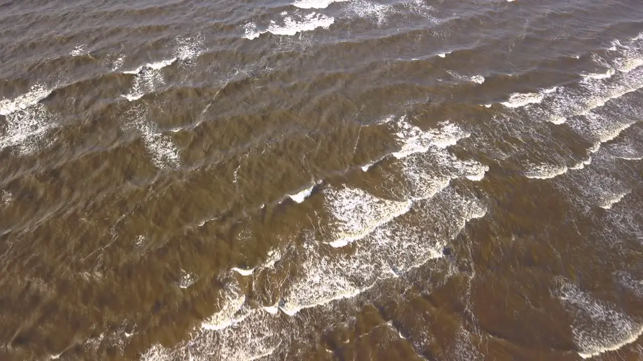 Aerial shot of waves crashing onto the beach dark murky sea water