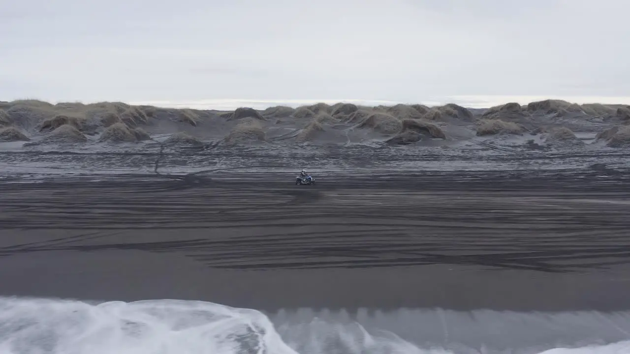 Lone quad biker travels on scenic black beach in cold Iceland truck right