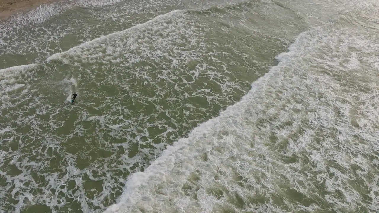 Establishing aerial birdseye view of a man engaged in kitesurfing overcast winter day high waves extreme sport Baltic Sea Karosta beach  drone shot moving forward