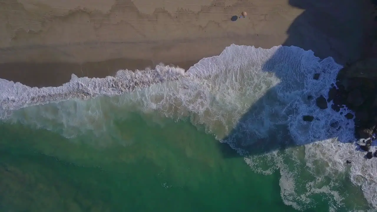 Slowmotion descending aerial shot of a stunning beach with waves crashing