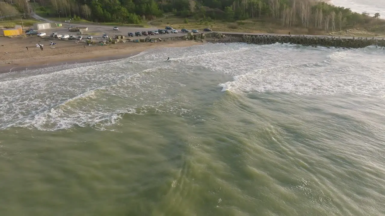 Establishing aerial view of a man engaged in kitesurfing overcast winter day high waves extreme sport Baltic Sea Karosta beach  drone shot moving forward