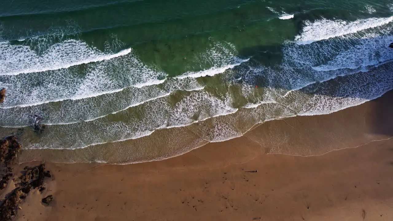 Static aerial looking down shot of waves hitting the beach in the morning Newquay Cornwall England Uk