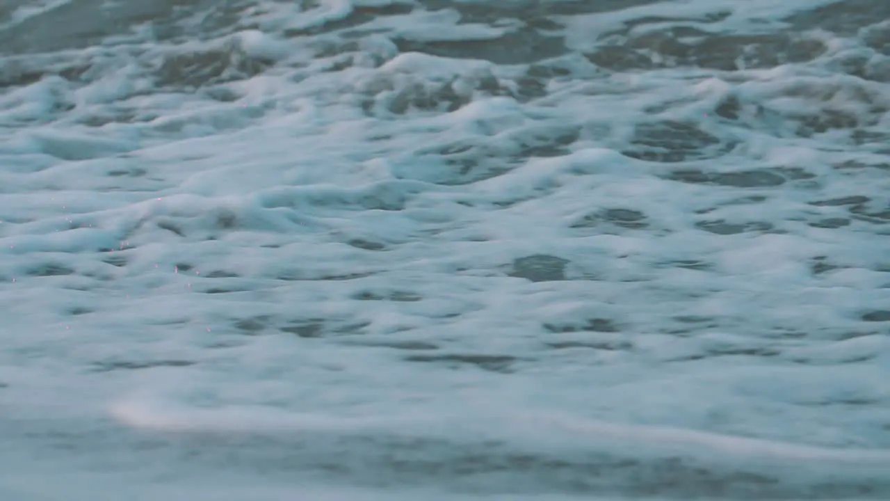 close-up of the foam of the waves crashing on the sand of the beach in slow-motion