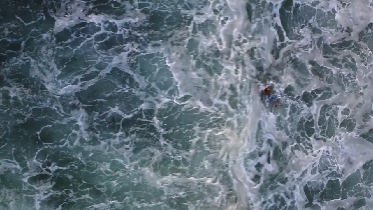 Aerial surfer paddling in breaking wave whitewater bird's eye view